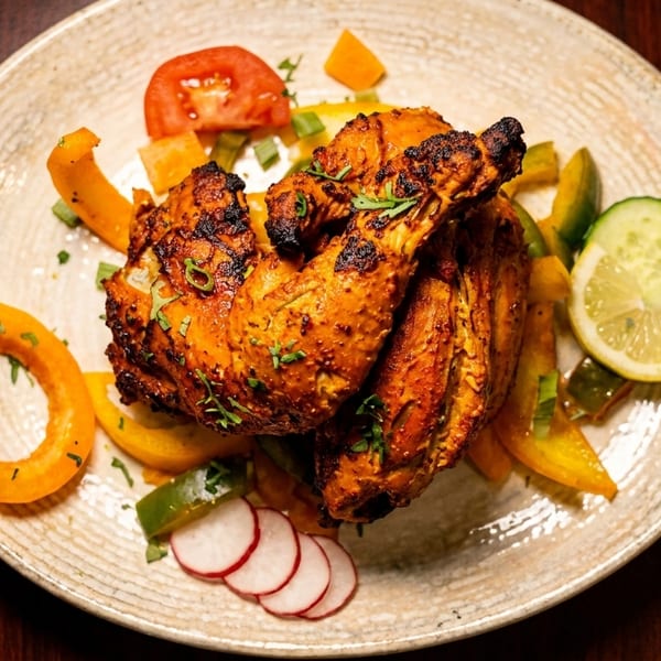 Grilled chicken with charred skin, bell peppers, tomato, cucumber, lemon, and radish on a plate.