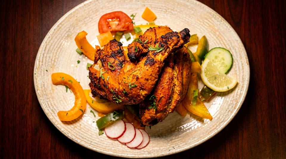 Grilled chicken with charred skin, bell peppers, tomato, cucumber, lemon, and radish on a plate.