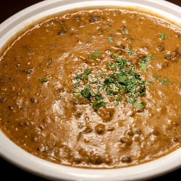 A white bowl filled with a rich, brown lentil curry, garnished with fresh green cilantro.