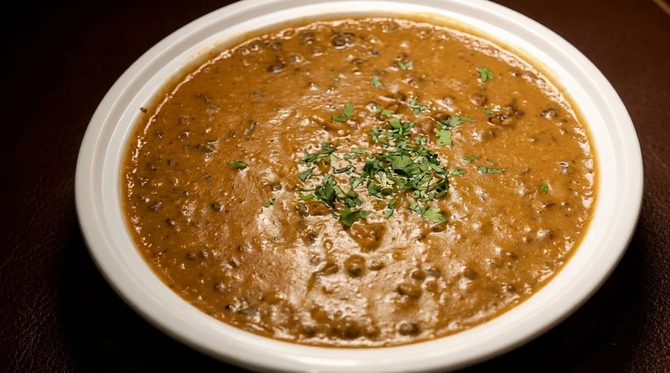 A white bowl filled with a rich, brown lentil curry, garnished with fresh green cilantro.