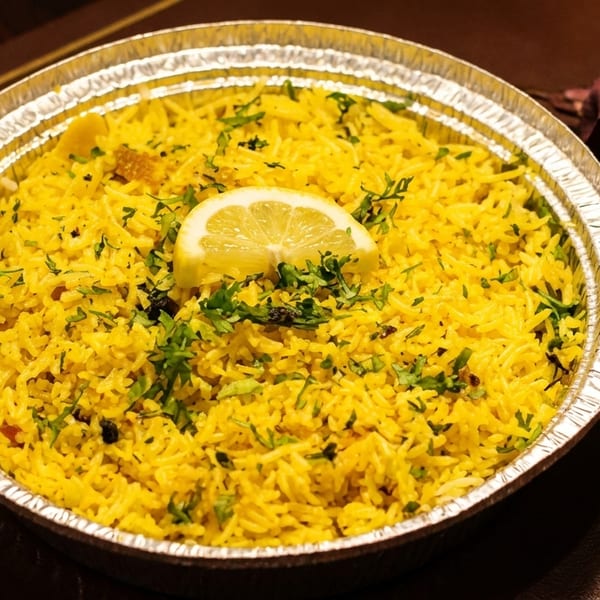 Yellow rice with herbs and a lemon slice in a foil container, next to a dark red rose.