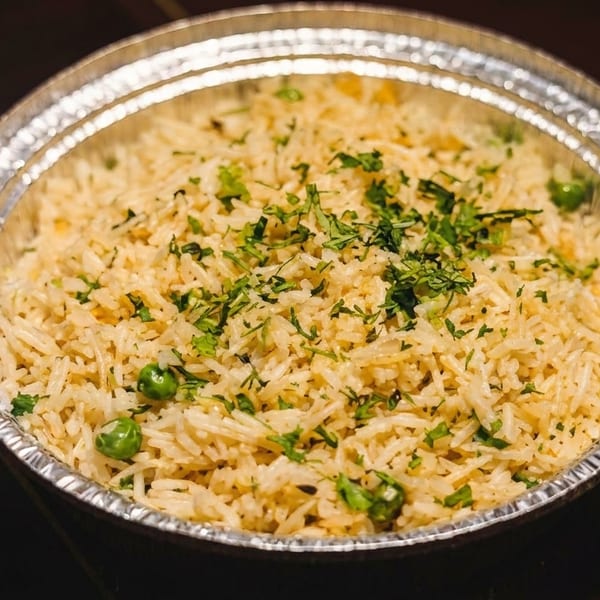 Fluffy rice with green peas and chopped herbs in a silver foil takeout container.