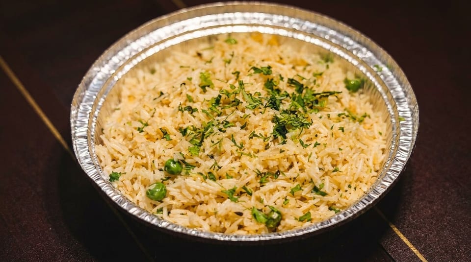 Fluffy rice with green peas and chopped herbs in a silver foil takeout container.